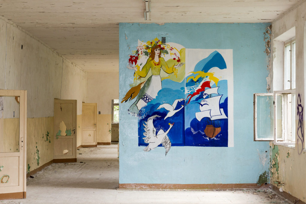 A school mural depicts a sailboat, its bright colours oddly out of place with the rather forlorn architecture.