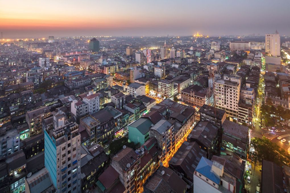 The context today. Yangon at dusk from the top of Centrepoint Towers. Downtown, the tight street grid dates from colonial days of the mid-19th century. On the horizon, glowing golden, is the Shwedagon Pagoda, Yangon&rsquo;s most famous landmark.