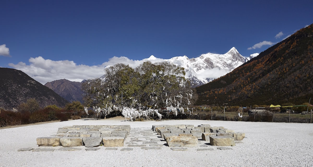 The place of contemplation in Tibet that standardarchitecture created by disposing roughly hewn boulders of local stone as seating in front of a panorama of a 1,300 year old mulberry tree backed by the 7,782 peak of the Namcha Barwa mountain.