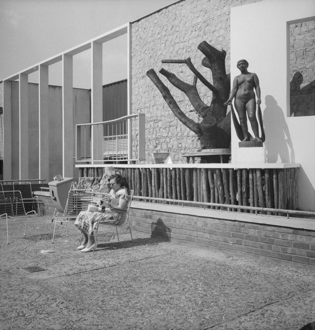 A visitor relaxes in front of the Homes and Gardens pavilion at the South Bank Exhibition during the Festival of Britain, 1951. (&copy; Historic England)