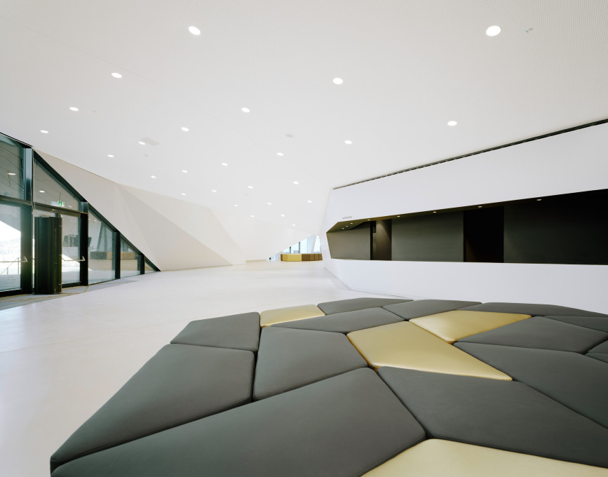 The foyers fluid spaces are composed of white walls, a light-colored floor, and dramatic geometry in all dimensions...