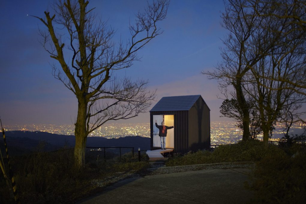 The curator of the exhibition&nbsp;&ldquo;Come on-a My Hut!&rdquo;, architect Yoshifumi Nakamura, standing at dusk in the doorway of one of his projects, Luna Hut in Hyogo, built in 2012.&nbsp;(Photo: Hideya Amemiya)
