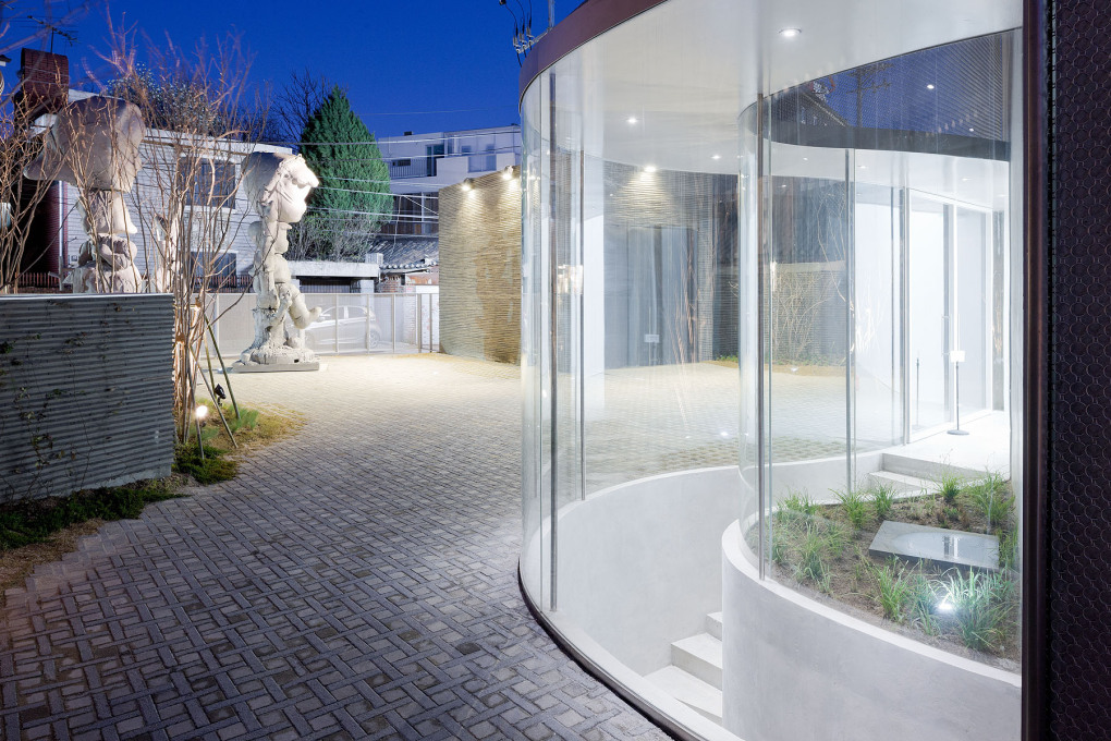 A curved glass wall reaches into the rear of the site, transparent yet impassable. (Photo: Iwan Baan)